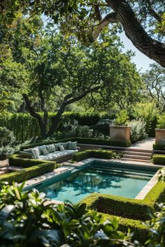 an outdoor swimming pool surrounded by hedges and trees with seating area in the middle,