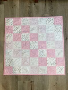 a pink and white patchwork quilt on a wooden floor