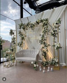 an outdoor wedding ceremony setup with white flowers and greenery on the back drop wall