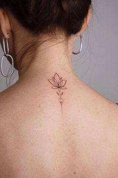 the back of a woman's neck with a small flower tattoo on her left side