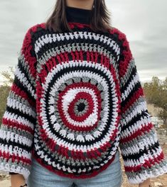 a woman wearing a red, white and black crocheted sweater with a spiral design