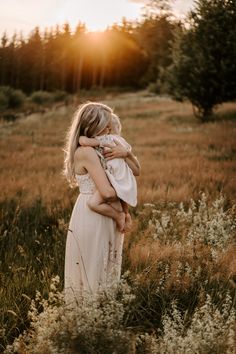 a woman holding a child in a field at sunset