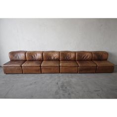 a brown leather couch sitting on top of a cement floor next to a white wall