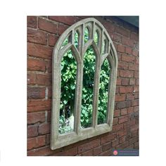 an arched window on the side of a brick wall with trees reflected in it's windowsill