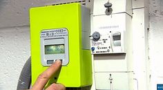 a hand points at an electronic meter on the wall next to a green box and fan