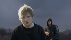 two young men standing next to each other in front of a dark sky with clouds