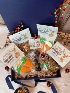 an assortment of treats in a gift box with blue ribbon and christmas decorations around it