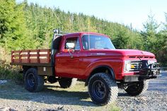 a red pick up truck parked on top of a gravel road next to some trees