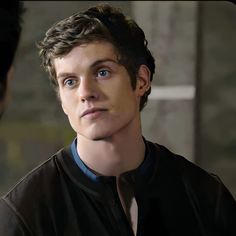 a young man with blue eyes stares into the distance as another looks on in the background