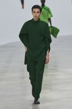 a model walks down the runway in a green outfit