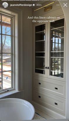 a white sink sitting in front of a window next to a wall mounted cabinet with glass doors