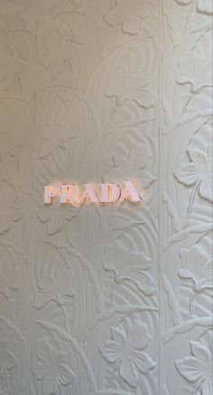 the word prada is illuminated in pink neon letters on a white textured wall