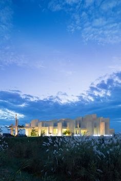 the building is lit up at night with clouds in the sky above it and grass on the ground