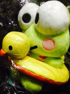 a green stuffed animal sitting on top of a plastic bag next to a yellow banana