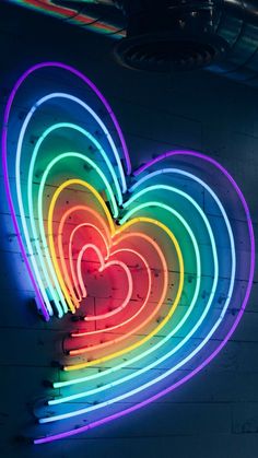 a heart shaped neon sign hanging on the side of a building