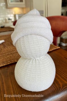 a white knitted snowman sitting on top of a wooden table next to a red chair