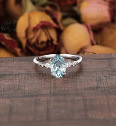 an oval aqua blue topazte and diamond ring on a wooden surface with roses in the background