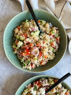 two bowls filled with rice and vegetables on top of a white tablecloth next to spoons