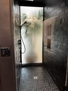 an open door leading to a bathroom with stone flooring and black tile on the walls