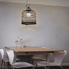 a birdcage hanging from the ceiling over a dining room table with four chairs