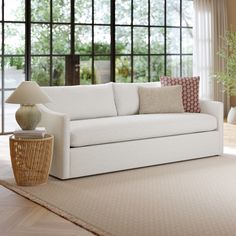 a white couch sitting on top of a wooden floor next to a table with a lamp