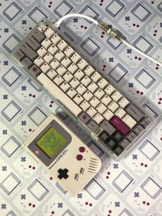 an old computer keyboard sitting on top of a table next to a small gameboy