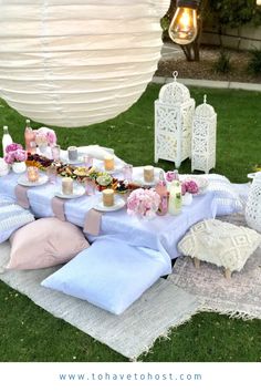 an outdoor picnic is set up on the grass with pink and white flowers, candles, and food