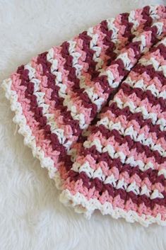 a pink and white crocheted dishcloth laying on top of a white blanket