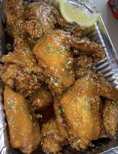 chicken wings with lemon wedges and parsley on top in a tin foil container