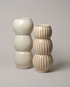 three white and brown striped vases sitting next to each other on a gray surface