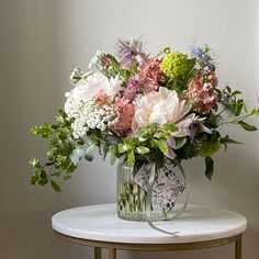 a vase filled with lots of flowers on top of a white table next to a window