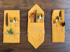 three folded napkins with forks and spoons in them on a wooden table top