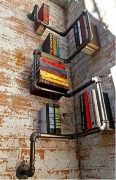 books are stacked up on the side of a brick wall with pipes running down it