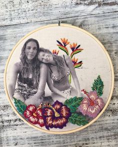 two women sitting next to each other in front of a flower embroidery pattern on a hoop