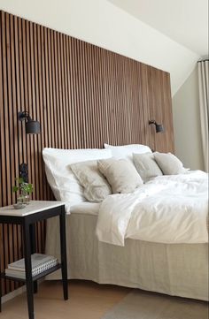 a bed with white linens and pillows in a bedroom next to a wooden wall