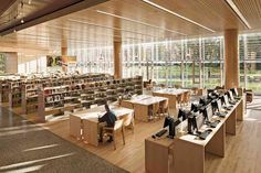 an empty library filled with lots of books and people sitting at desks in front of large windows