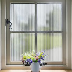 a white mug filled with flowers sitting on top of a window sill next to a window