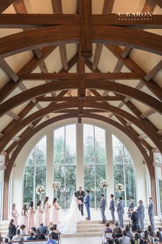 the wedding party is standing at the alter in front of the large window with lots of windows