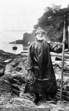 an old black and white photo of a man standing on rocks with a pole in his hand