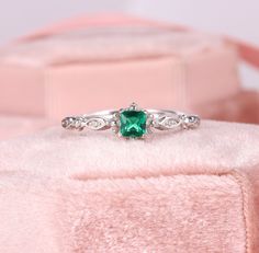 a ring with a green stone in it sitting on top of a pink velvet box