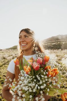 a woman holding a bouquet of flowers in her hands and smiling at the camera with sun shining on her face