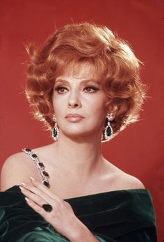 a woman with red hair and earrings posing for a photo in front of a red background