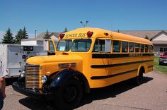 an old school bus parked in a parking lot next to other vehicles and people standing around