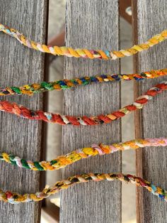 multicolored bracelets are hanging on a wooden fence with string attached to them