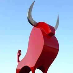 a large red bull statue sitting on top of a lush green field next to a blue sky