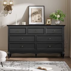 a room with a white chair, black dresser and pictures on the wall above it