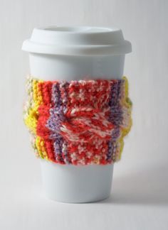 a coffee cup with a knitted sleeve on it's side, sitting on a white surface