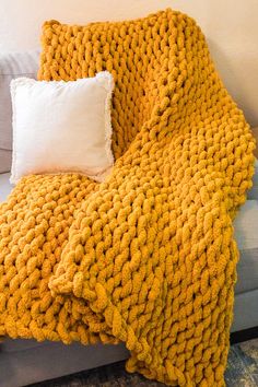 a yellow knitted blanket sitting on top of a couch next to a white pillow