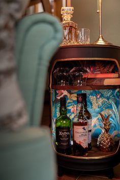 an assortment of liquor bottles and glasses sitting on top of a table next to a blue chair