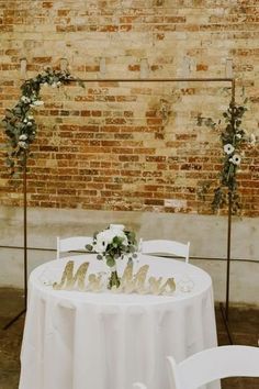 the table is set with white linens and flowers on it, along with two chairs